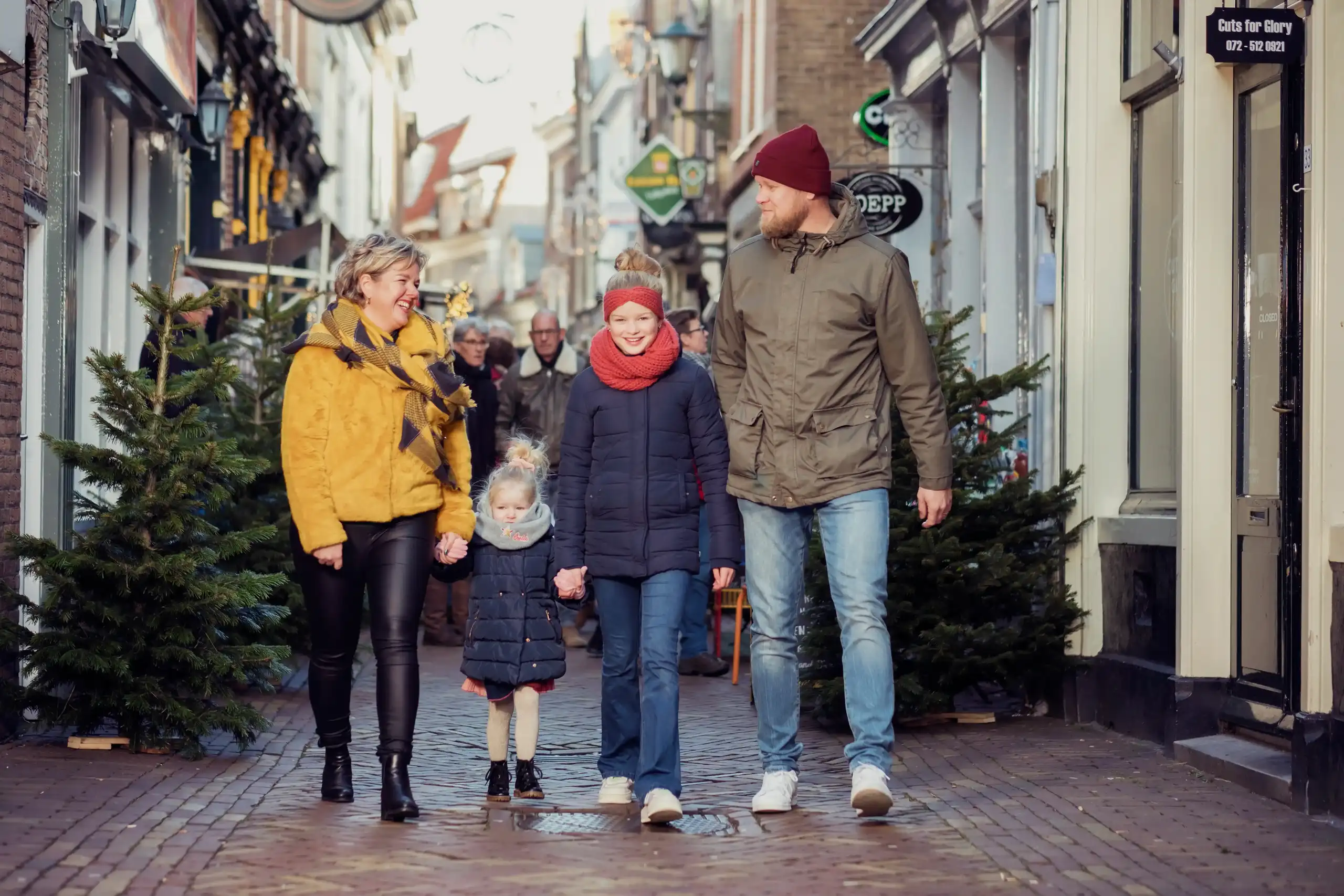 Gezin aan het winkelen met kerstbomen achter zich